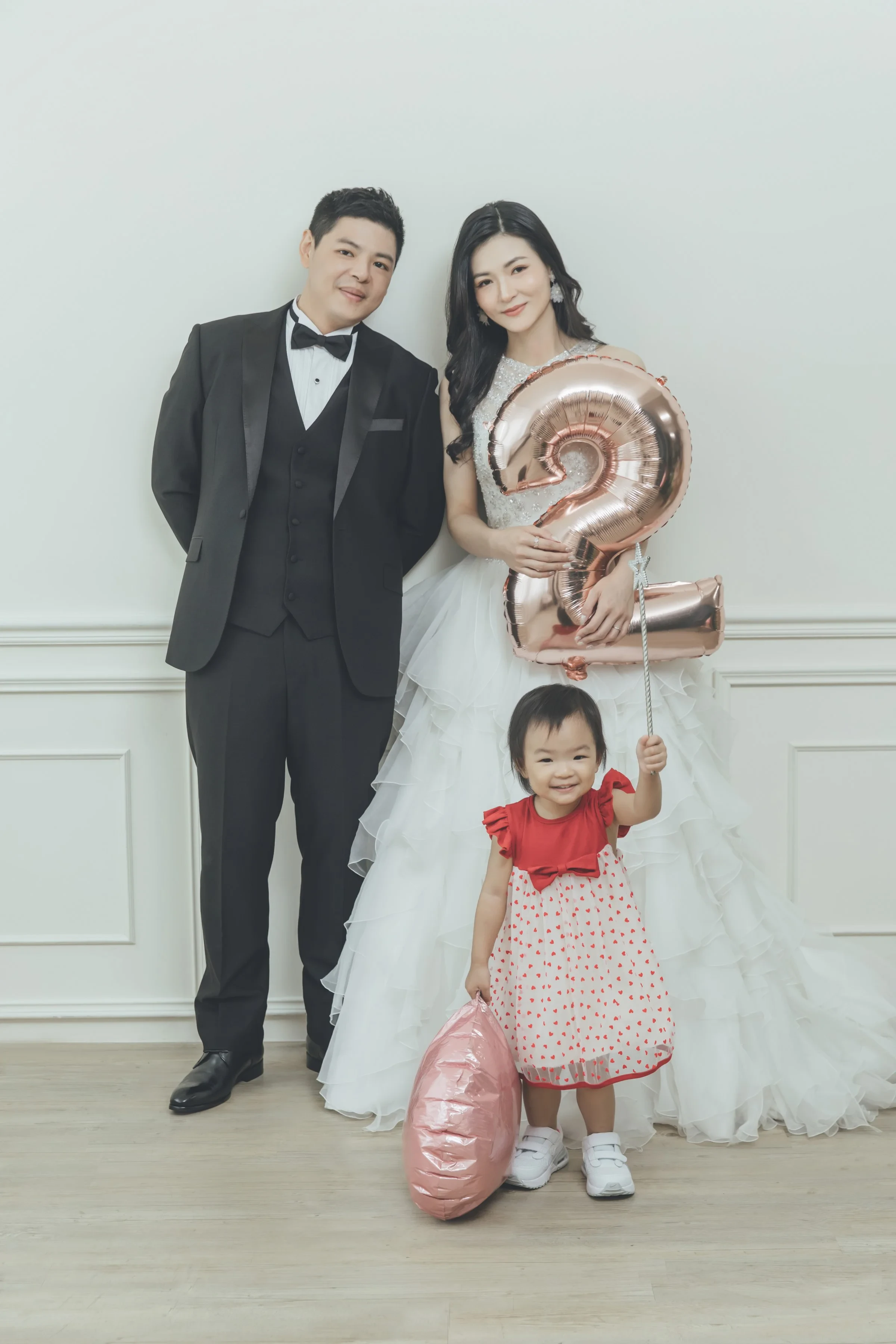 爸爸穿西裝、媽媽穿白紗，兩歲的女兒拿著數字 2 氣球